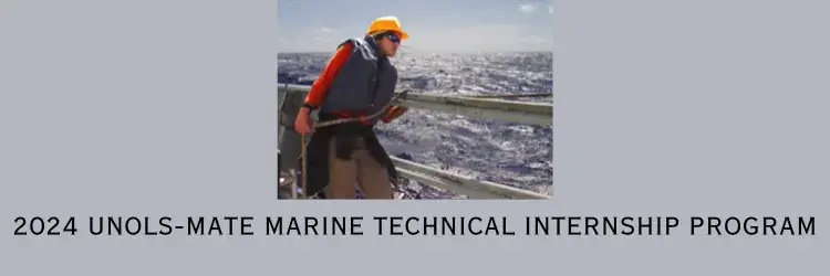 Person leaning on a ship's rail wearing a life jacket and hard hat with the background of a gray sea